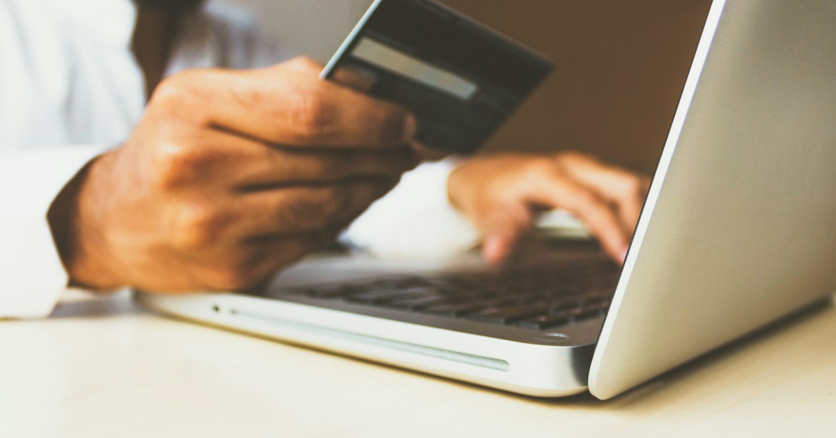 Personne tenant une carte bancaire devant un ordinateur portable ouvert, en train de consulter ses comptes en ligne